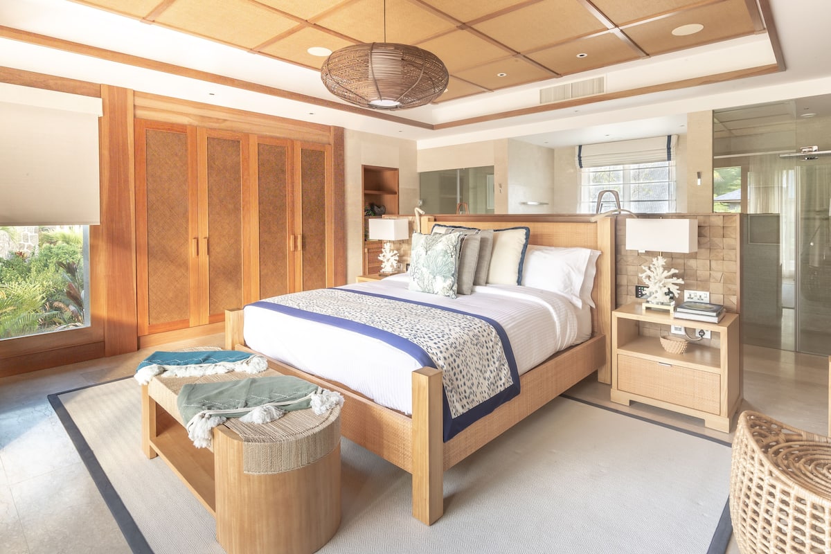A bedroom with a large bed, wooden wardrobe, bedside tables, and a view of greenery outside.