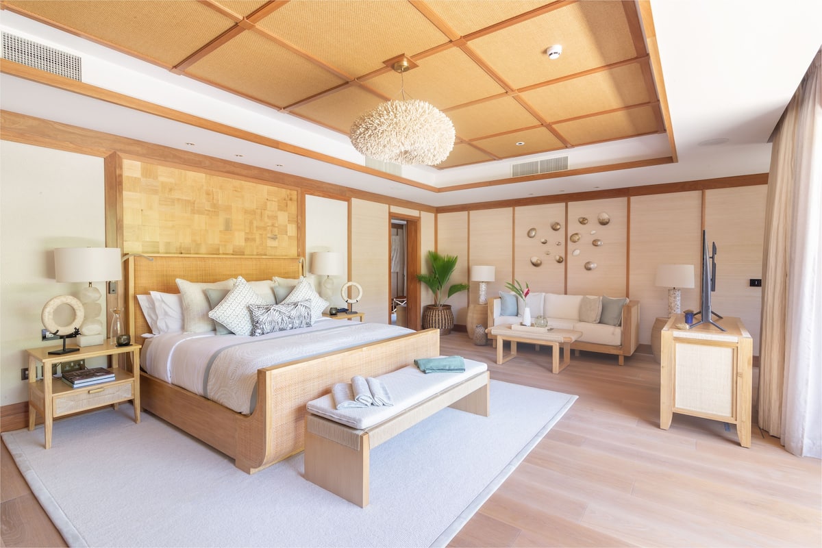 A spacious bedroom with a large bed, bedside tables, a bench, a sofa, and a TV.