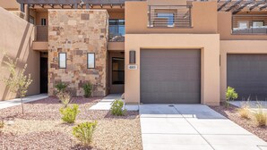 A modern two-story house with a stone facade, a garage, and a small garden area with gravel and plants. - Pleasant View (St. George)