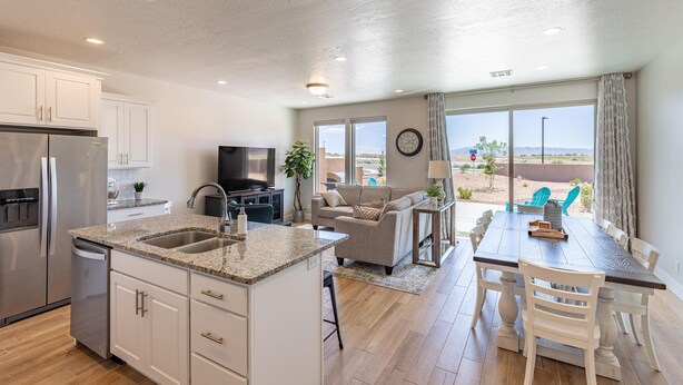 A modern kitchen with granite countertops, white cabinetry, and stainless steel appliances. There is a dining area with a wooden table and chairs, and a view of the desert landscape through large windows. - Pleasant View (St. George)