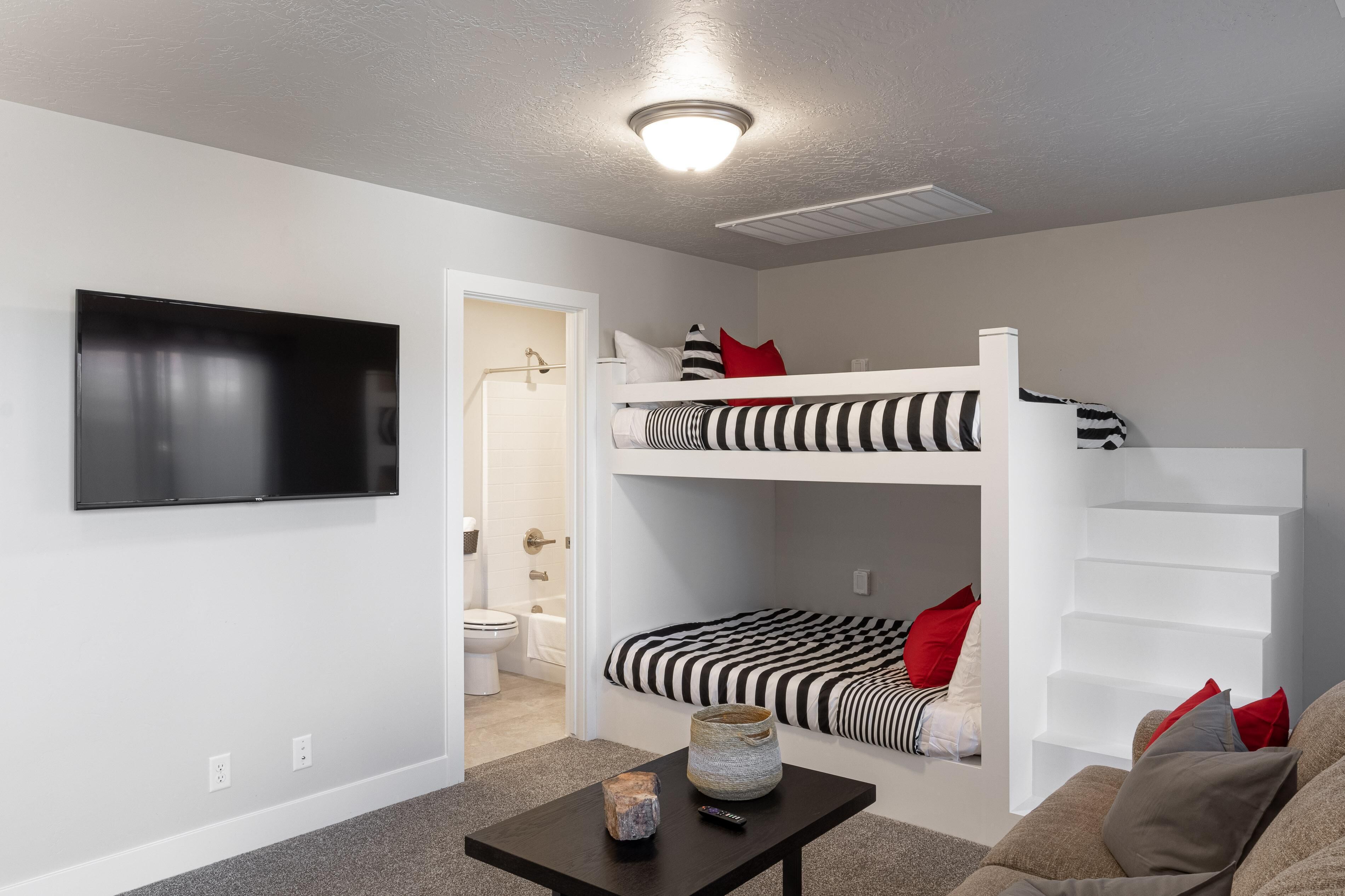 A modern, compact living space with a bunk bed, a flat-screen TV, and a small table with a vase and remote.