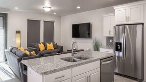 A modern kitchen with a stainless steel refrigerator, granite countertop, and a built-in dishwasher. - Solara Escape (St. George)