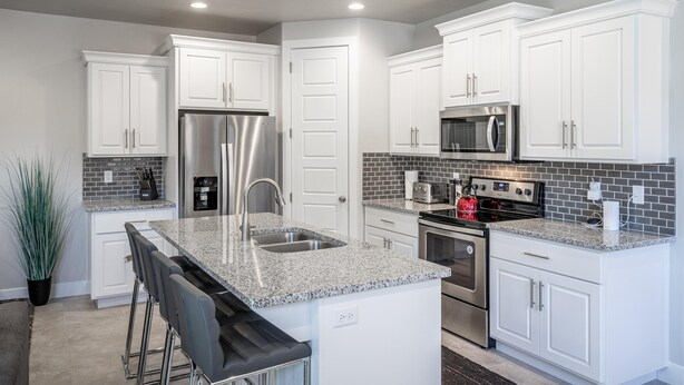 A modern kitchen with white cabinets, stainless steel appliances, a granite countertop, and a bar stool area. - Solara Escape (St. George)