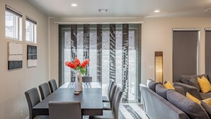 A modern living room with a dining table, sofa, and large windows with blinds. - Solara Escape (St. George)