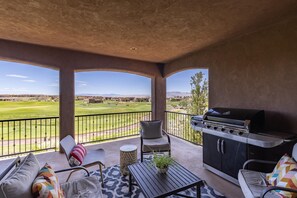 A balcony with a grill, seating, and a view of a golf course.