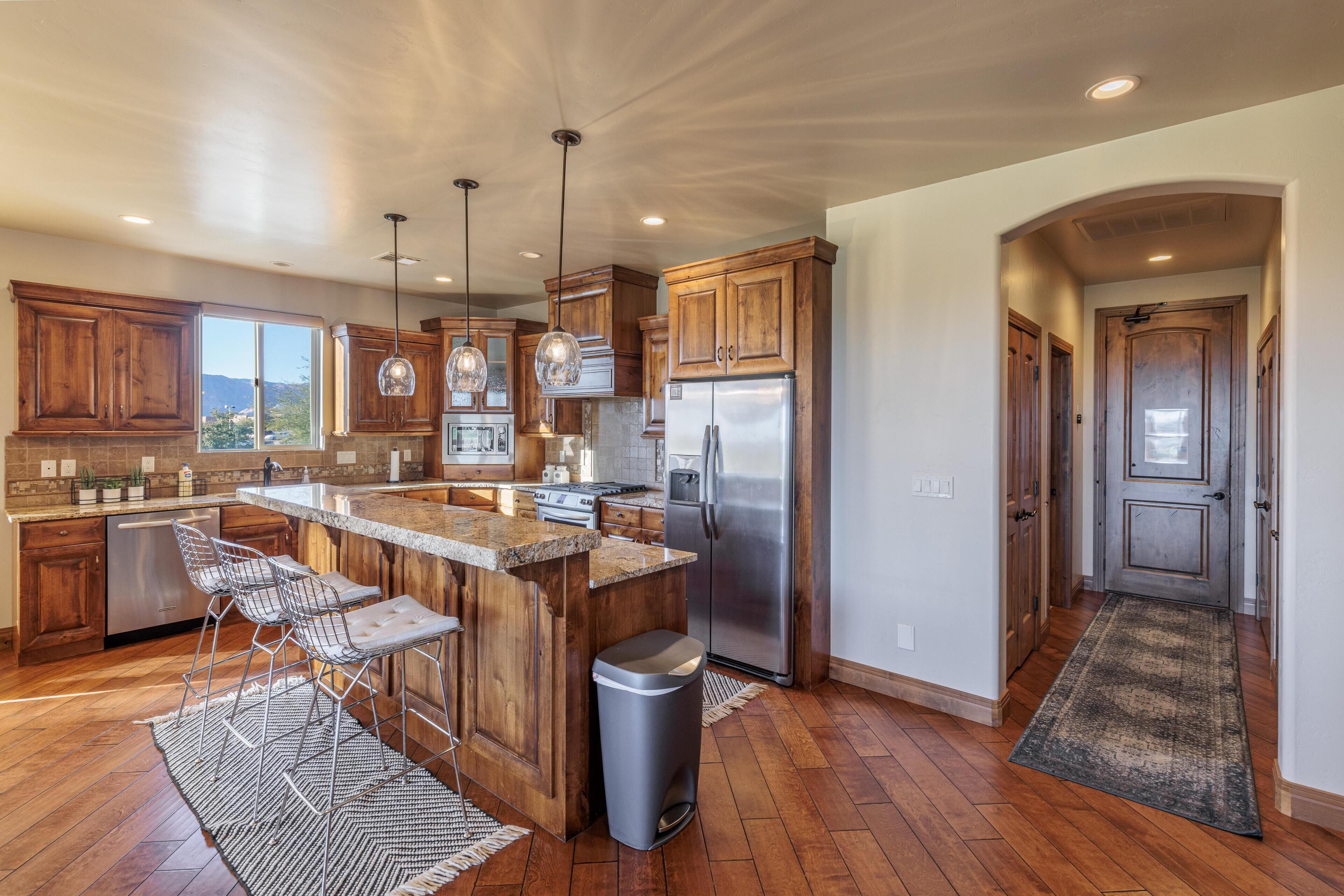 A kitchen with wooden cabinets, stainless steel appliances, and a bar area with stools.