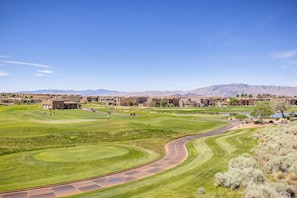 A golf course with a winding path, buildings in the background, and mountains in the distance.