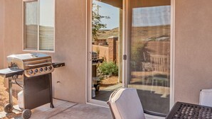 A patio with a grill, a sliding glass door, and a view of a backyard.