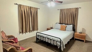 Un dormitorio con cama, mesitas de noche, una silla y un ventilador de techo.