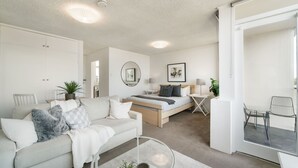 Ein modernes, helles Wohnzimmer mit einer Couch, einem Couchtisch und einem Bett mit einem Nachttisch.