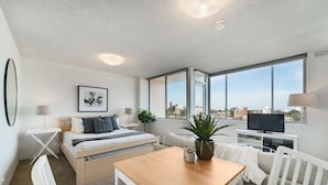 Ein modernes Hotelzimmer mit Bett, Schreibtisch, Fernseher und großen Fenstern mit Blick auf die Stadt.
