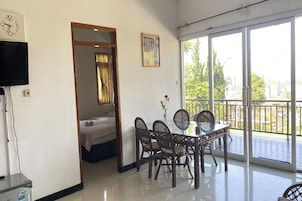 Una habitación con cama, una mesa de comedor con sillas, un televisor y un balcón con vistas a zonas verdes.