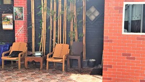 A small outdoor seating area with two wooden chairs and a table, bamboo plants, and a tiled floor. - Katawa Guest House Syariah (Palembang)