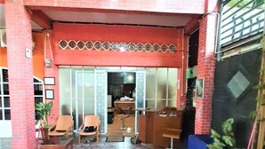 A red brick building with a tiled entrance, a reception desk, and several chairs outside. - Katawa Guest House Syariah (Palembang)