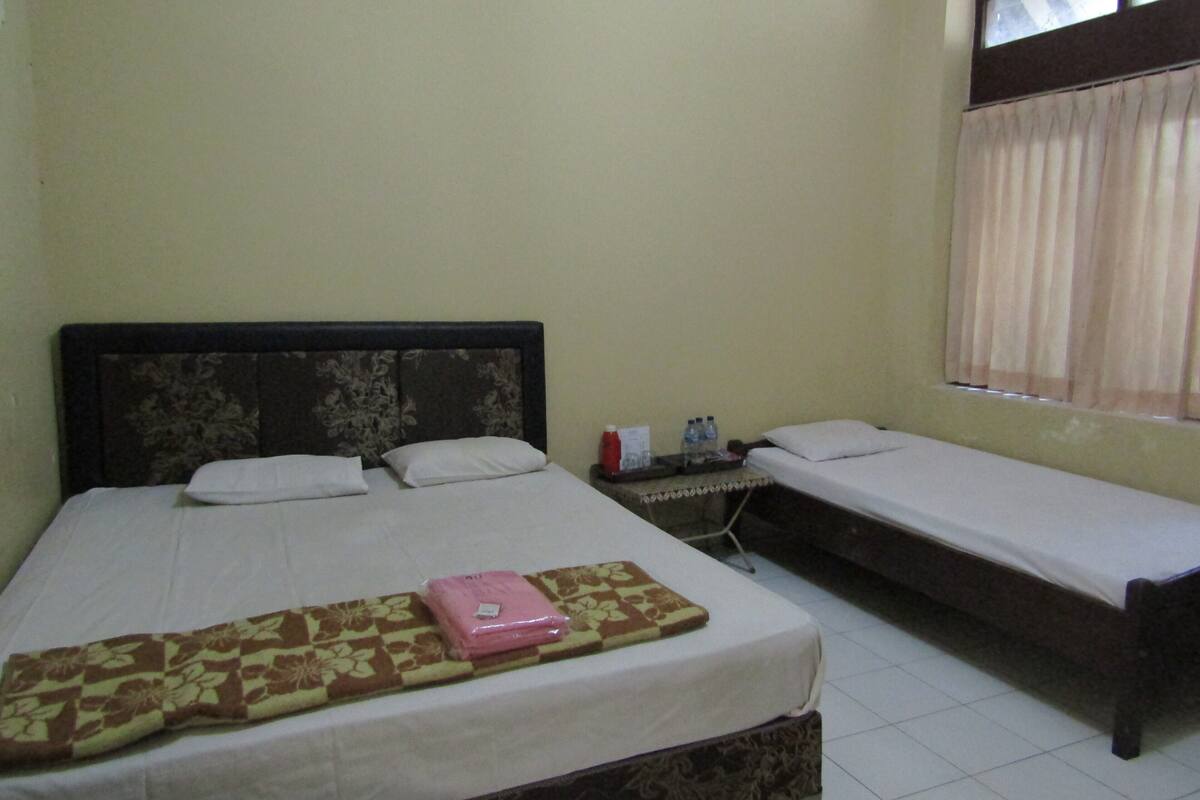 A room with two single beds, a bedside table with a lamp, and a window with curtains.