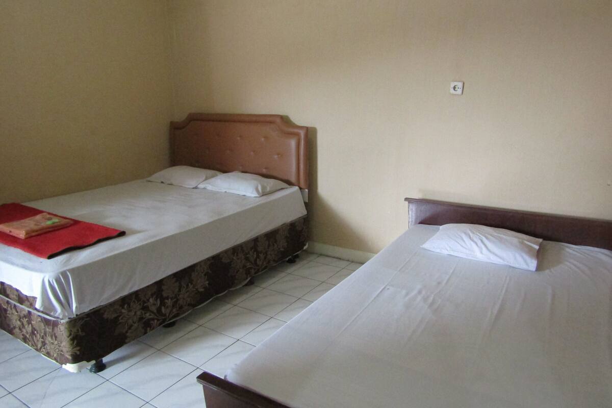 A room with two beds, one with a floral-patterned bedspread and the other with a plain white bedspread.