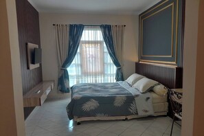 Ein Schlafzimmer mit Bett, einem an der Wand befestigten Fernseher, einem Fenster mit Vorhängen und einer Holzbank.