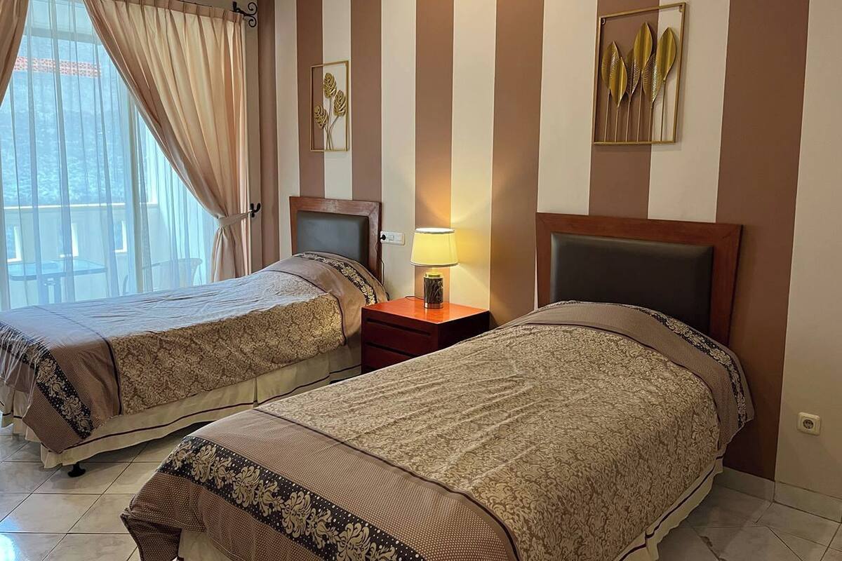 Ein Hotelzimmer mit zwei Betten, gestreifter Wandgestaltung, einem Fenster mit Vorhängen, einem Nachttisch mit Lampe und einem Bild an der Wand.