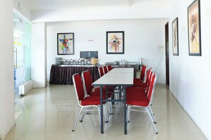 A conference room with a white table and red chairs, a buffet area in the background, and artwork on the walls.