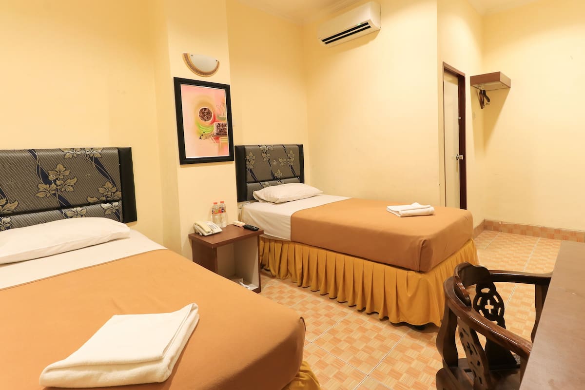A hotel room with two beds, a bedside table with a phone, a wall-mounted air conditioner, and a framed picture.