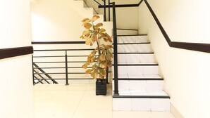A staircase with black railings and white steps, a potted plant, and a tiled floor. - Al-badar Hotel Syariah Makassar by Zuzu (Makassar)