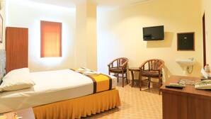 A hotel room with a bed, two chairs, a desk with a telephone and remote controls, a television mounted on the wall, and a window with a curtain. - Al-badar Hotel Syariah Makassar by Zuzu (Makassar)
