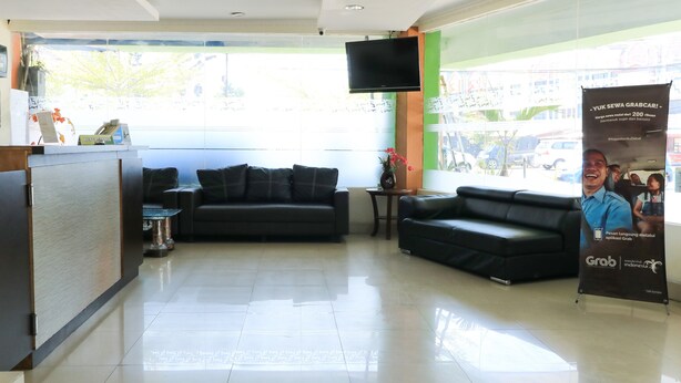 A reception area with a black leather sofa, a small table, and a TV mounted on the wall. - Al-badar Hotel Syariah Makassar by Zuzu (Makassar)