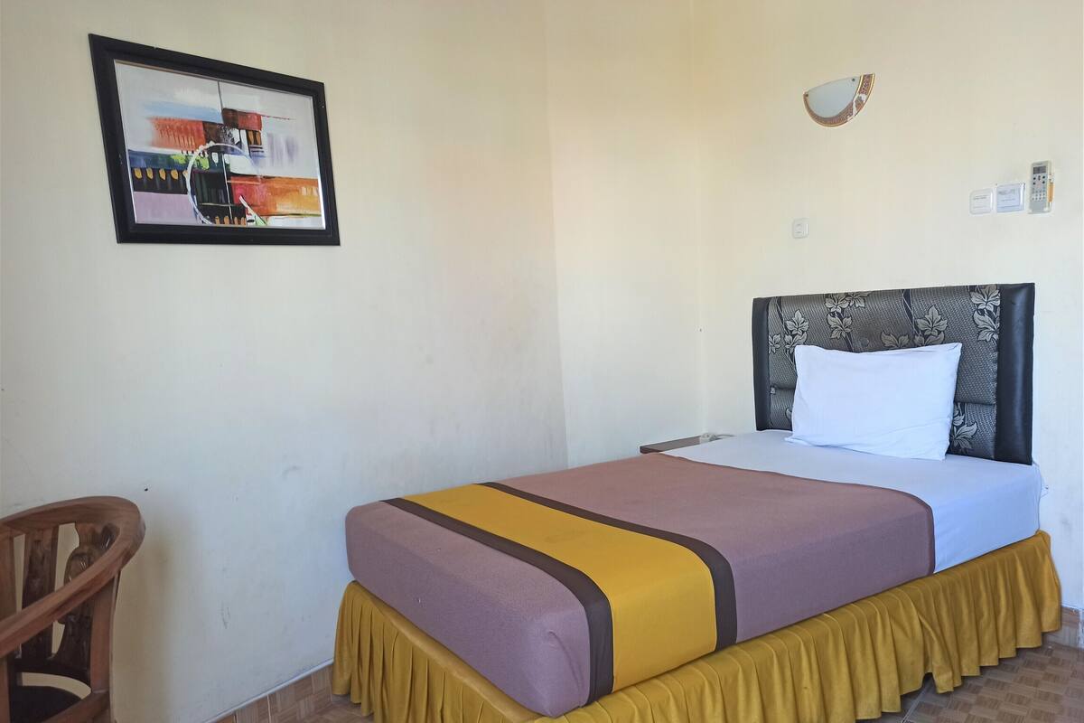 A hotel room with a bed, a chair, a wall-mounted light, and a framed picture.