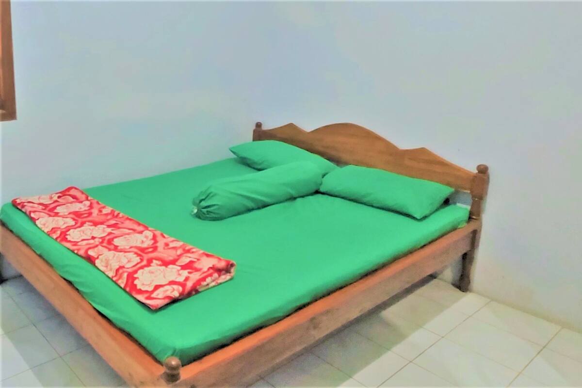 A single-bed room with a wooden frame, green bedding, and a red patterned throw.
