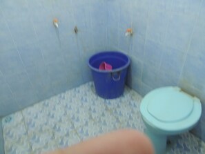 A bathroom with a blue toilet, a blue bucket, and a patterned floor. - Wisma Artha (Ngaglik)