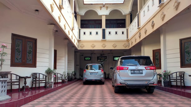L’entrée d’un hôtel, avec un sol à carreaux, deux voitures garées et un escalier menant à l’étage supérieur.