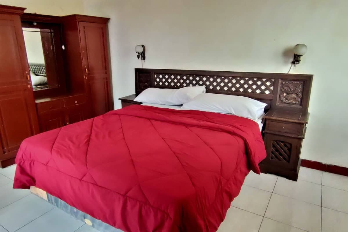 Une chambre à coucher avec un lit, une armoire en bois, une table de chevet et une lampe fixée au mur.