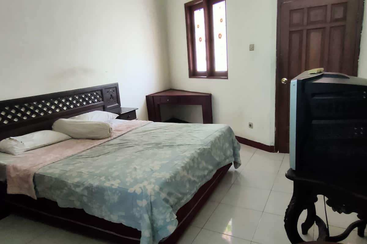 Une chambre à coucher avec un lit, un petit bureau, une télévision et une fenêtre.