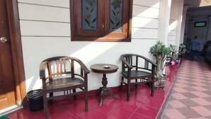 Une entrée d’immeuble avec deux chaises en bois et une petite table, une plante en pot et une voiture garée.