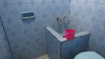 A bathroom with blue patterned tiles, a pink bucket, a small blue soap dish, and a toilet.