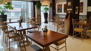 A modern cafe with wooden tables and chairs, large windows, and indoor plants. - Festive Hotel Makati (Makati)