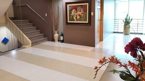 A spacious lobby with a staircase, a framed painting, and potted plants. - Festive Hotel Makati (Makati)