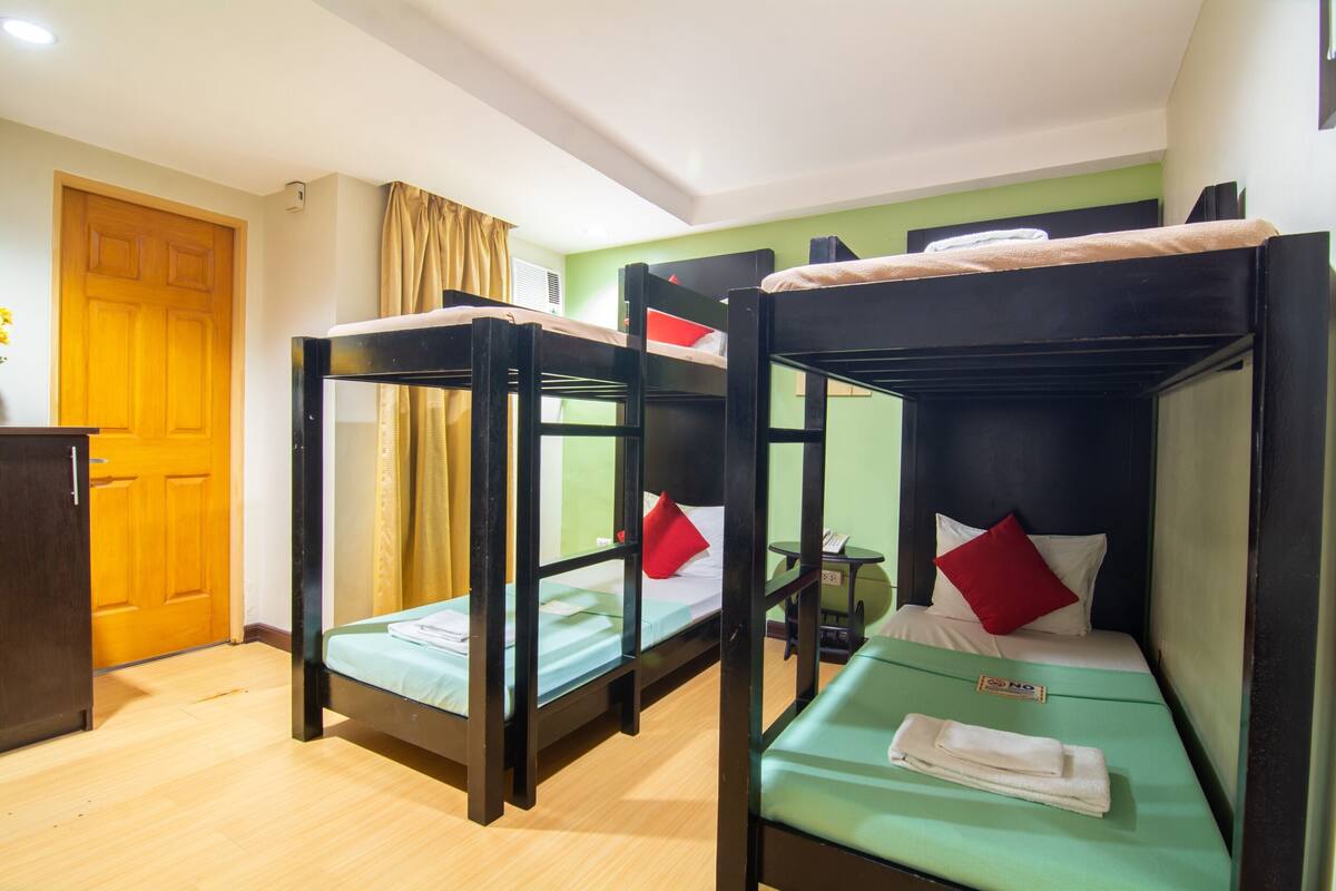 Quarto com beliches, porta de madeira, uma mesinha e parede verde.