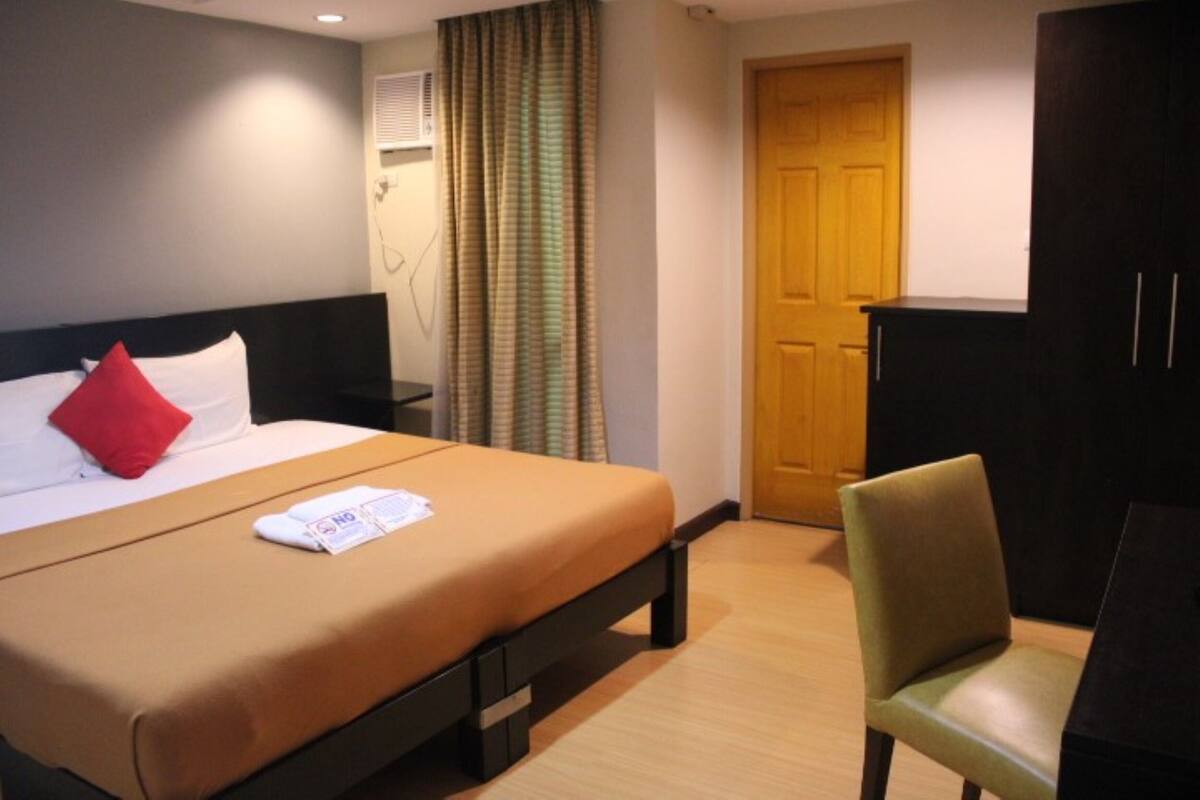 Quarto de hotel com cama, escrivaninha, cadeira, guarda-roupa e porta.