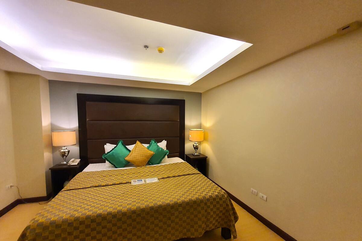 Quarto de hotel com uma cama grande, duas mesas de cabeceira com luminárias, uma cabeceira e um claraboia.