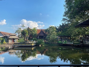 A tranquil riverside setting with traditional buildings, a small boat docked on the water, and lush greenery. - Viewdoi Art and Resort (Chiang Mai)
