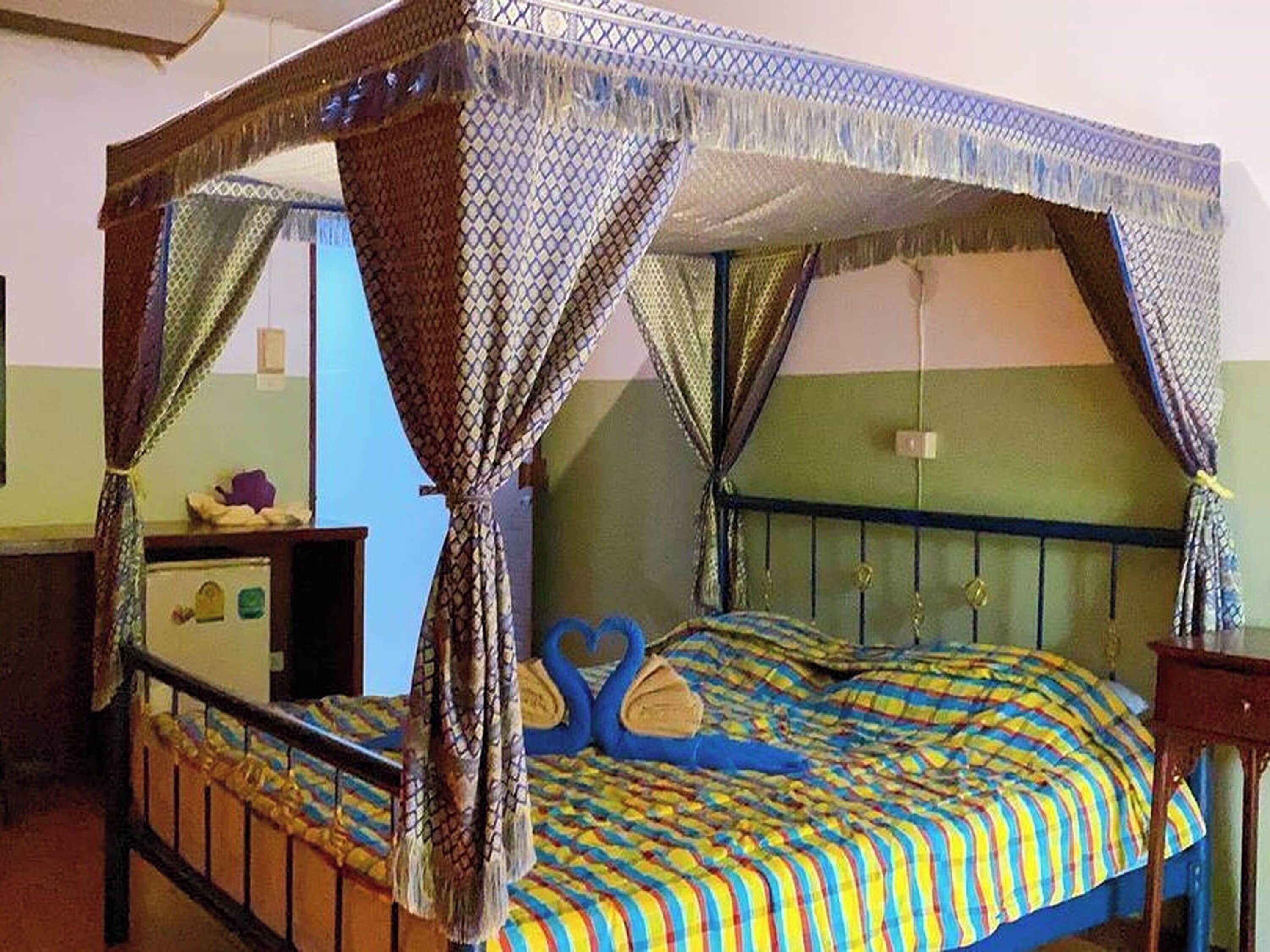 Un lit à baldaquin, une couverture colorée à rayures et une tête de lit ornée d’un motif en forme de cœur.