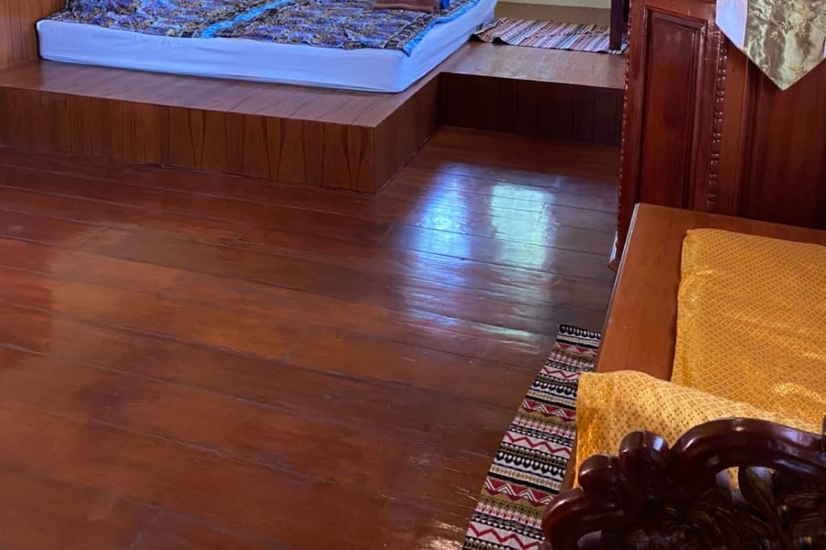 A room with a bed, a small table, a window with curtains, and a painting on the wall.