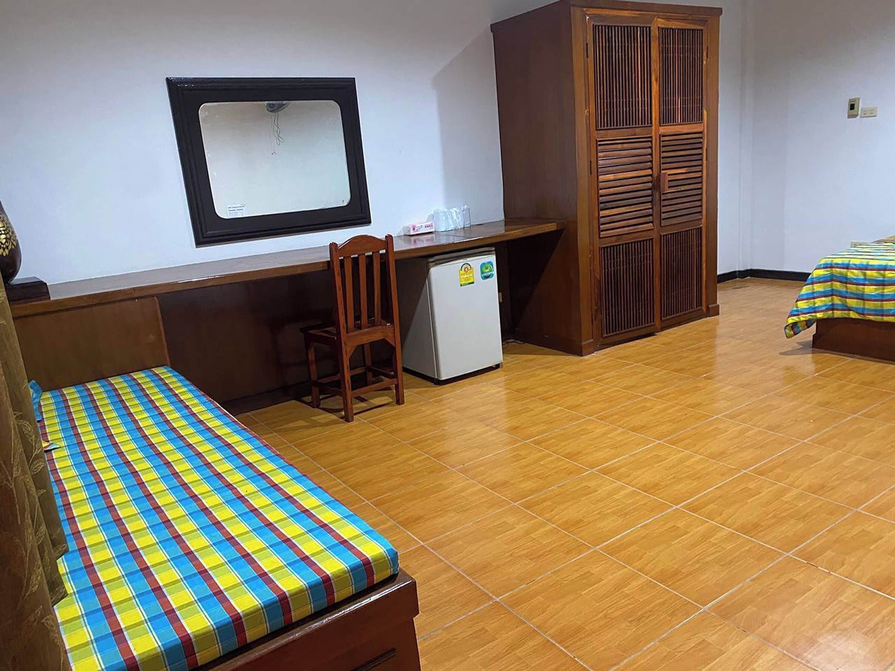A small, compact room with a wooden desk, a chair, a bed with a colorful bedspread, and a wardrobe.