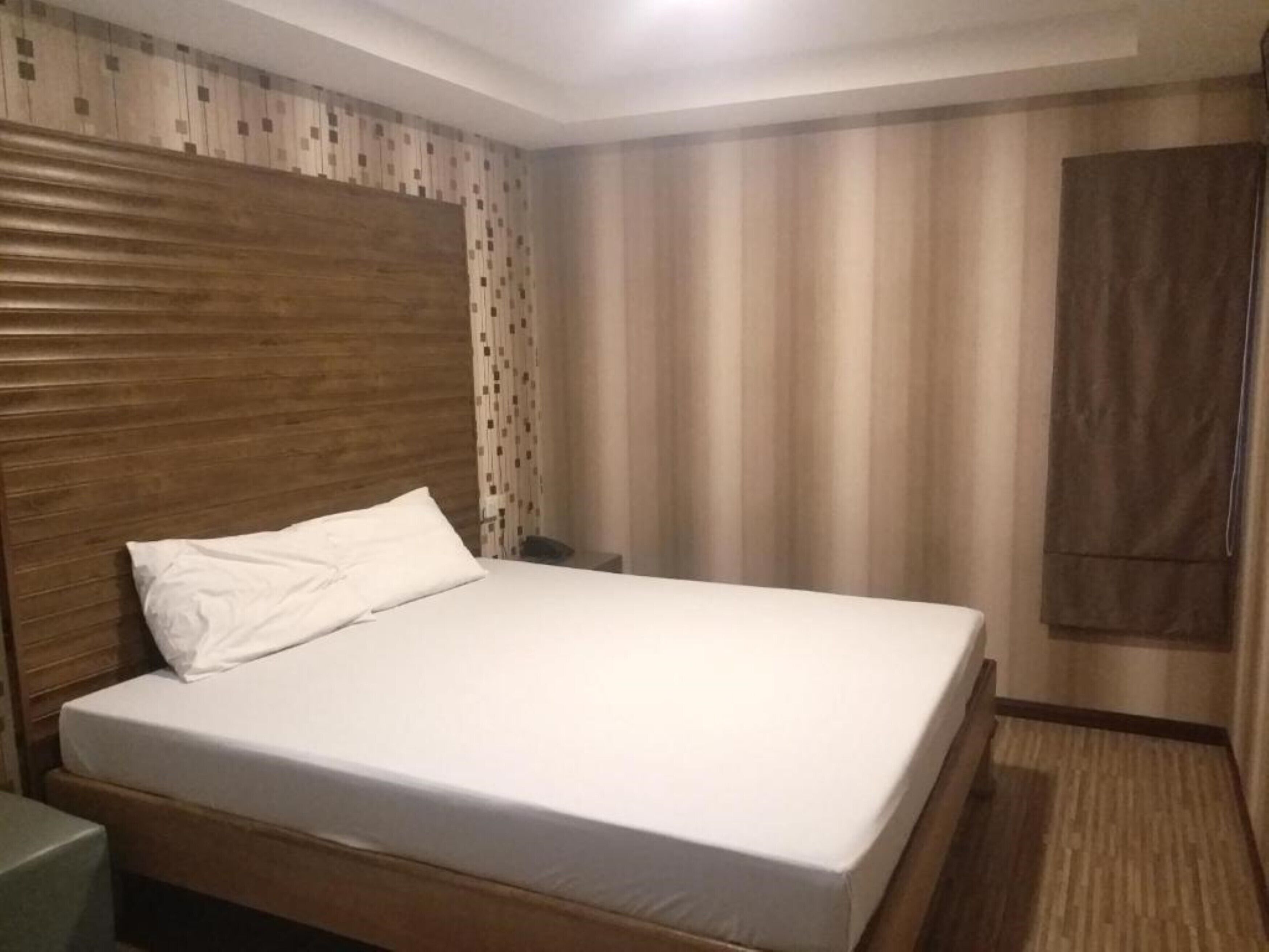 A single bed with a wooden headboard, a bedside table, and a curtain.