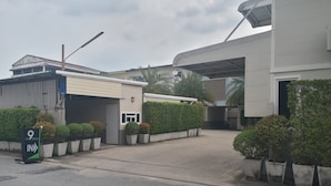 A hotel entrance with a covered driveway, a sign for The 9 IN, and a parking area with potted plants. - The 9 Resort (Bangkok)