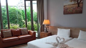 A hotel room with a bed, a sofa, and a window with a view of greenery. - Areeca Mahogany Zone (Choeng Thale)