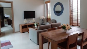 A modern living room with a sofa, a wooden dining table, and a TV. - Areeca Mahogany Zone (Choeng Thale)