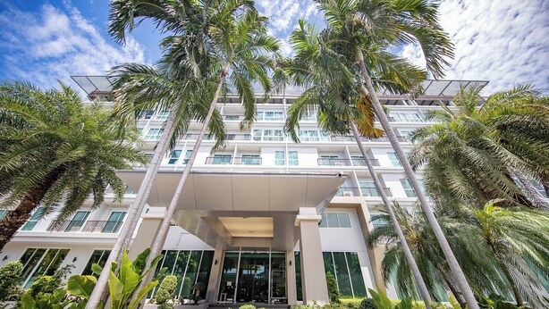 A multi-story hotel with a modern design, featuring a prominent entrance with a covered walkway, surrounded by lush tropical vegetation.