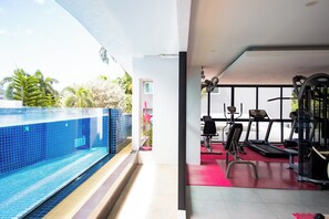 A modern gym with exercise equipment and a pool area. - Phavina Grand Boutique (Rayong)